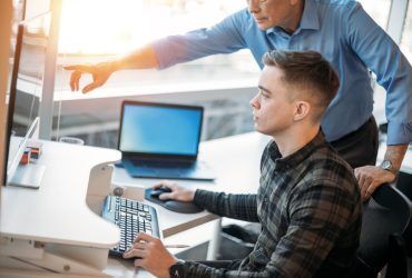 colleague-mentoring-younger-associate-in-business-office-while-pointing-at-data-on-computer-monitor